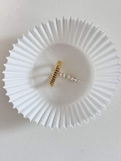 Overhead studio shot of the Callie moissanite eternity ring balanced perpendicularly inside a slim vede gold ribbed dome band on a white baking paper cup
