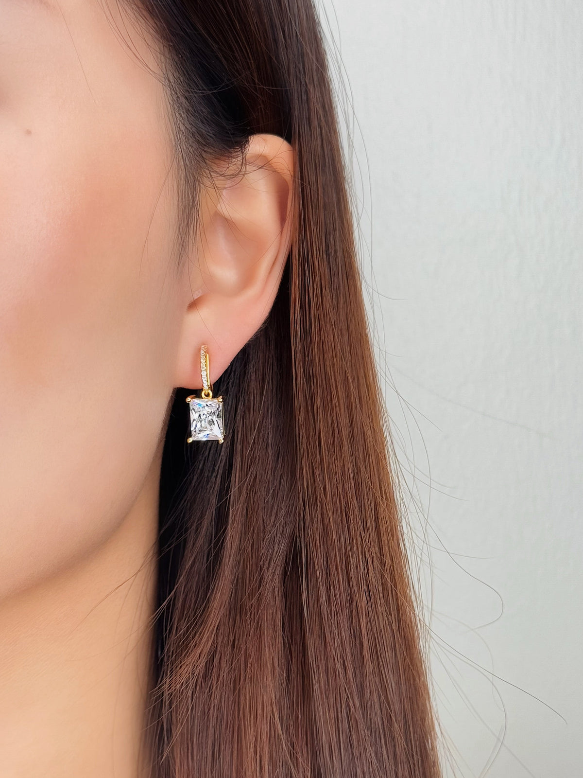 Model with sleek brown hair wearing Candice gold drop clip-on earrings in natural light