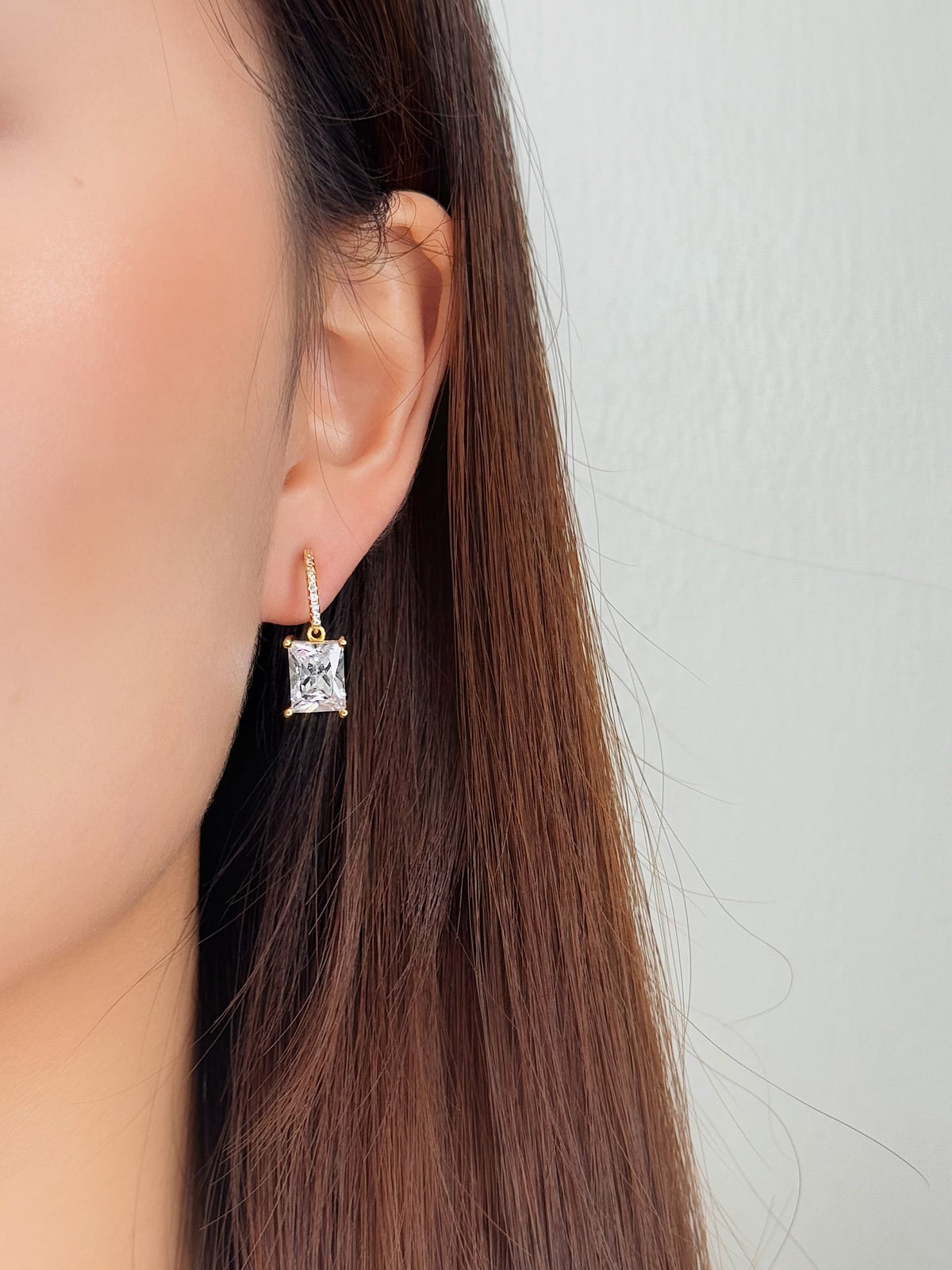 Close-up of model wearing 14K gold plated emerald cut drop clip-on earrings