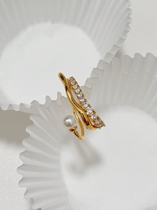 Top-down product shot of the elegant Cassidy Gold Cuff Earring resting on white fluted paper, showcasing its delicate freshwater pearl and pave-set crystal bridge design.