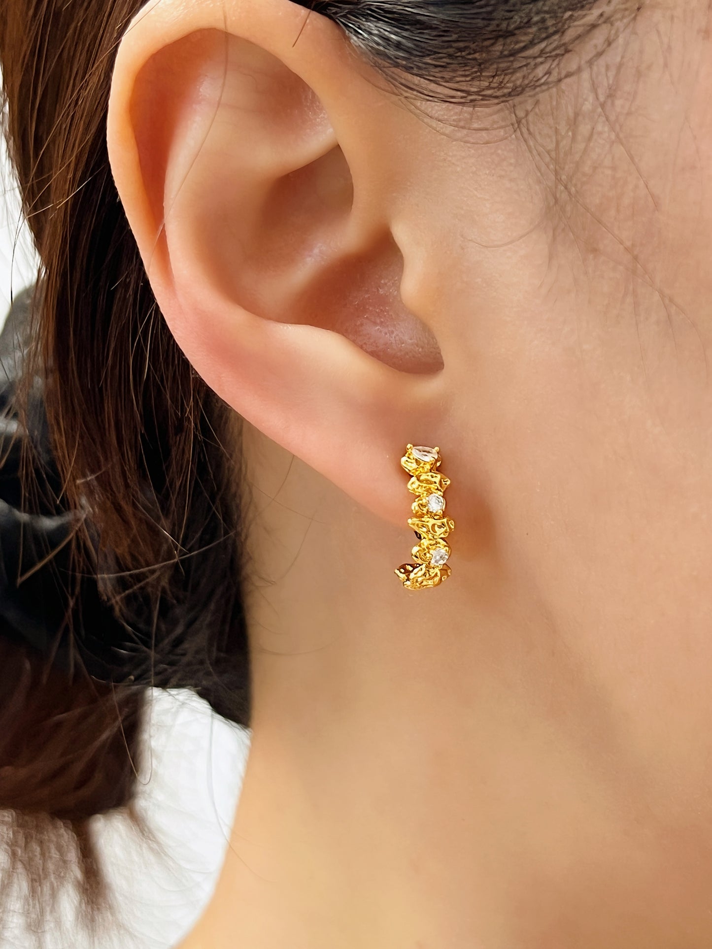 Side angle close-up of the Celeste Astral Climber Clip-on Earrings on model, showcasing the molten gold textured finish and sparkling crystal accents hugging the lobe.