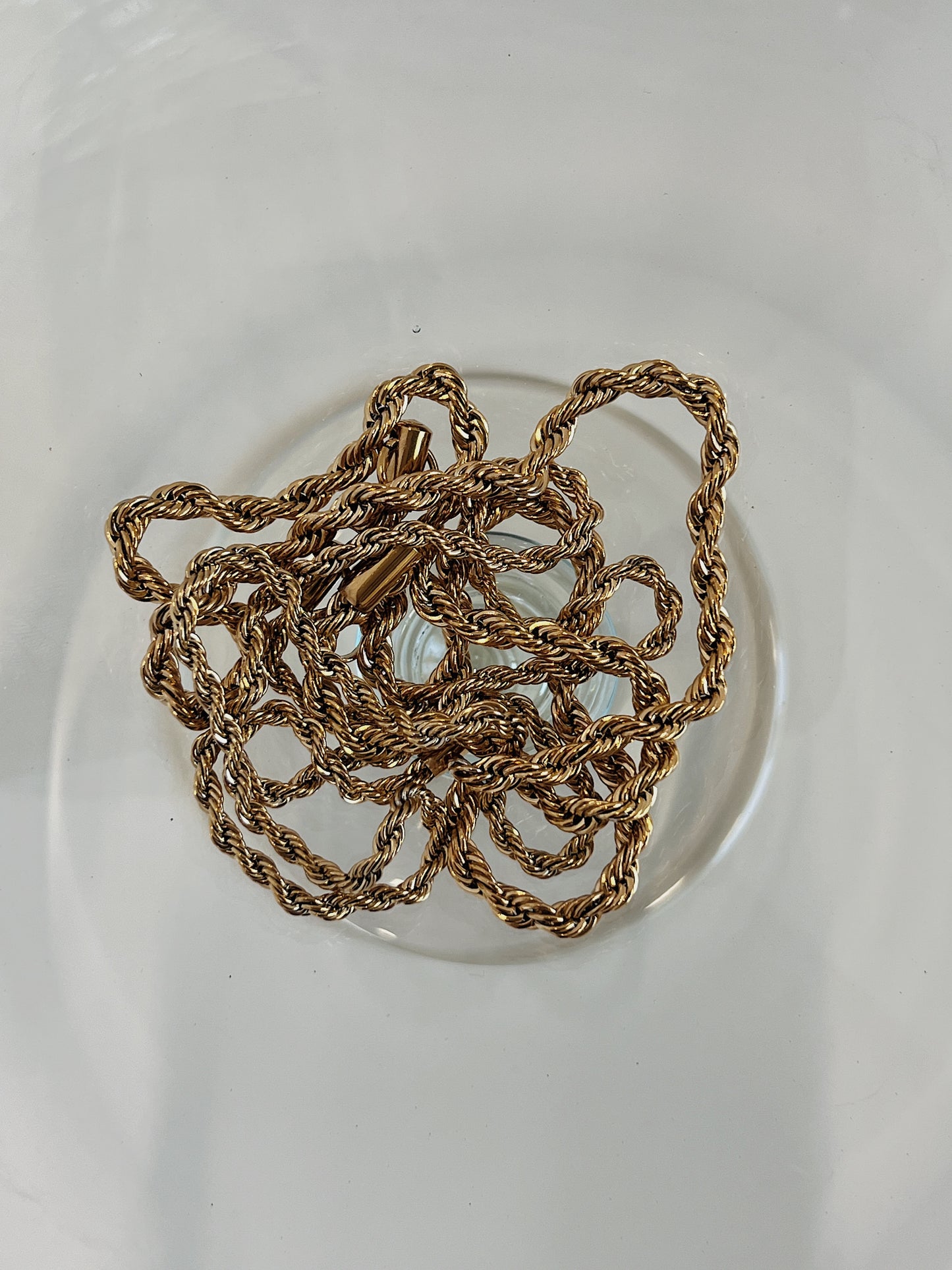 Chelsea gold twisted rope chain necklace resting on plain glass surface
