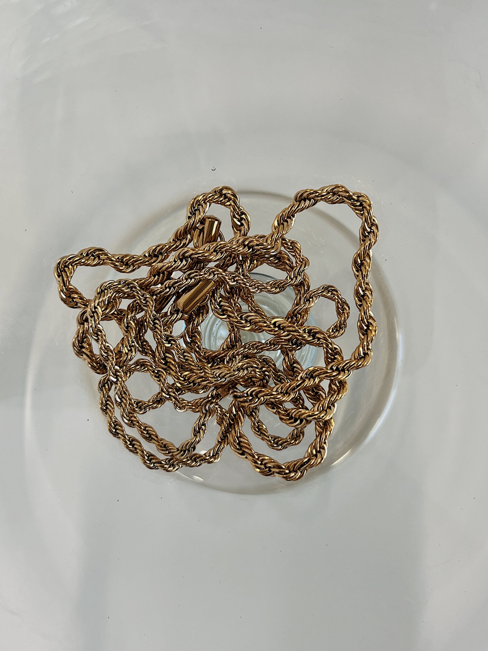 Chelsea gold twisted rope chain necklace resting on plain glass surface