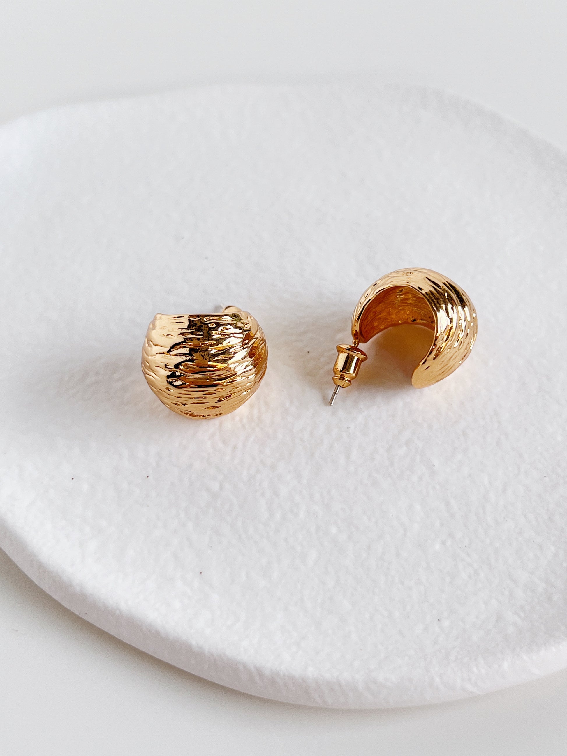 Close-up of Mira Gold Hoops on a white surface showing tactile ripple texture
