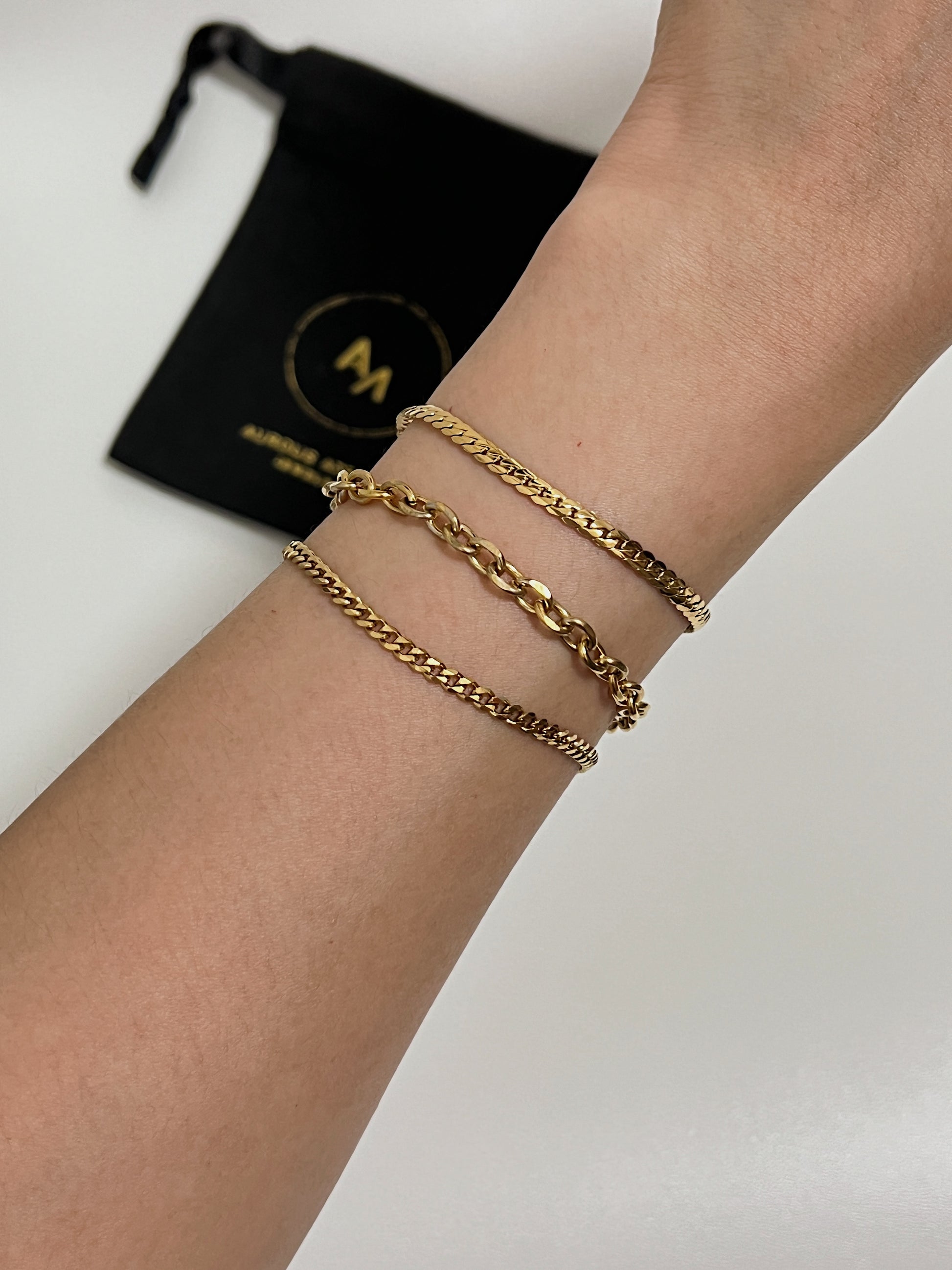 Model's wrist styled in a three-piece gold stack featuring the Trixie cable chain bracelet prominently in the center.