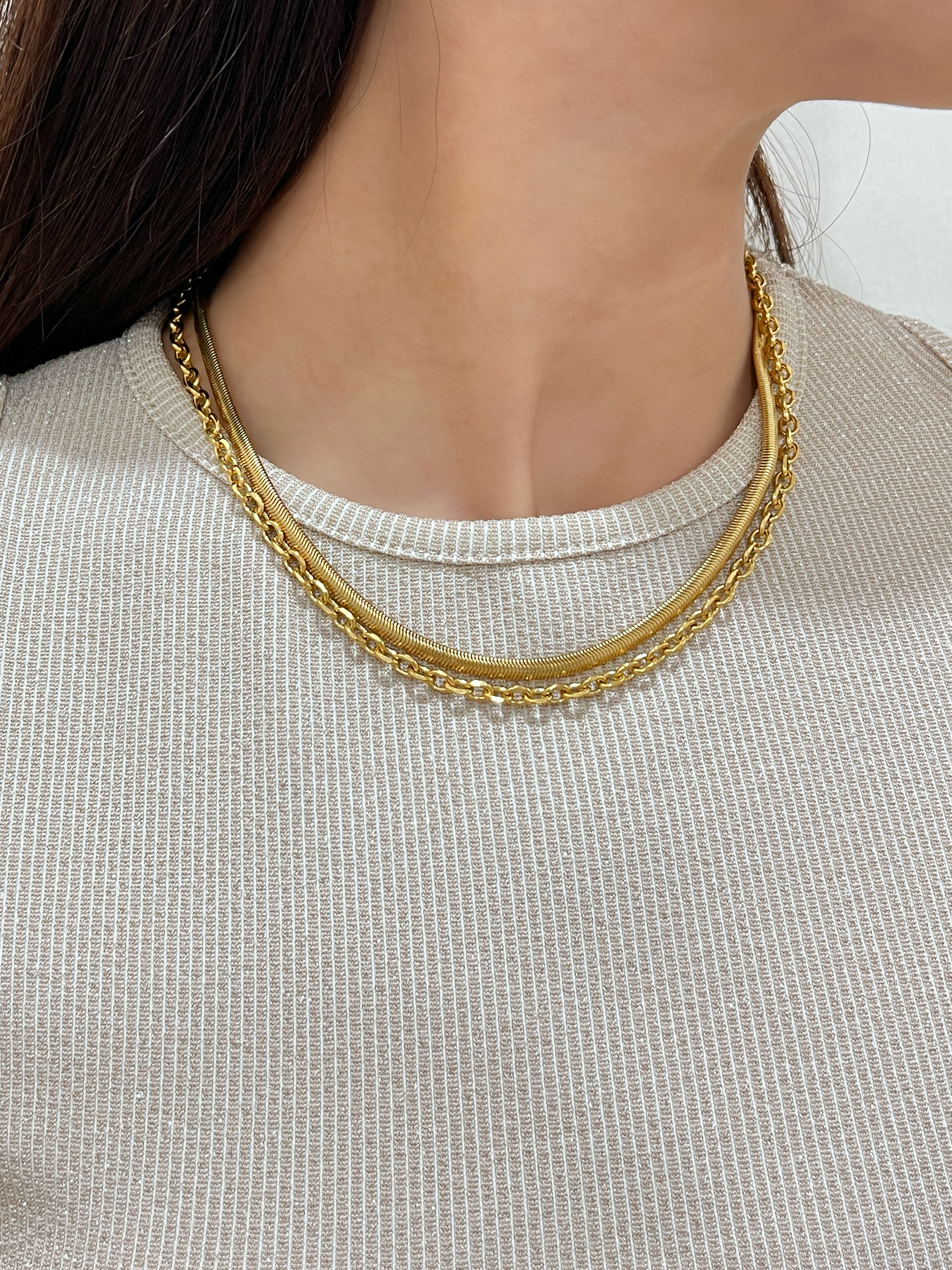 Model wearing the Trixie cable chain layered elegantly with a flat gold herringbone necklace on a beige top