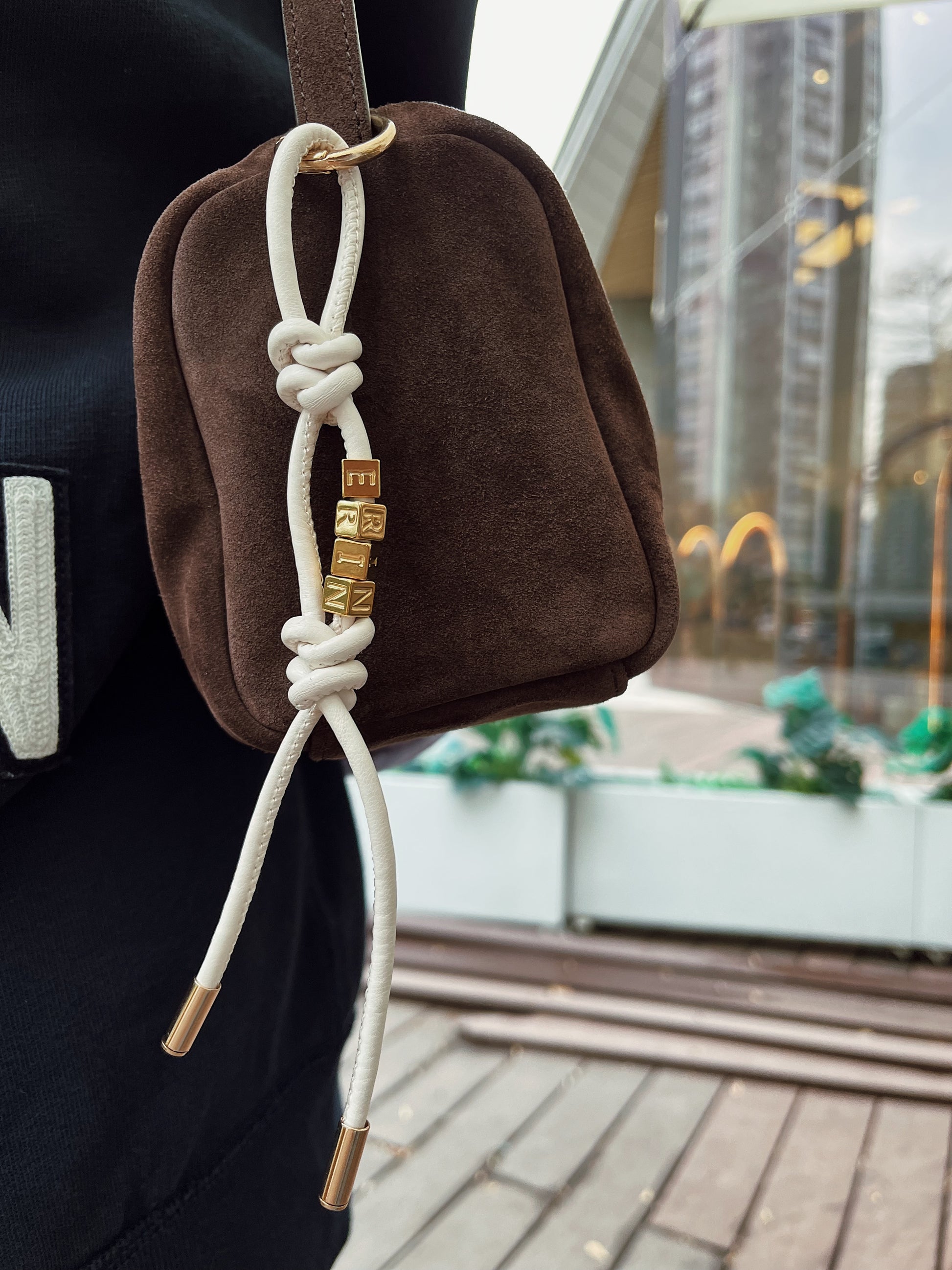 Model clipping personalized leather charm onto handbag.