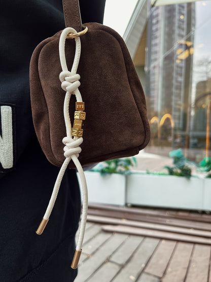 Model clipping personalized leather charm onto handbag.