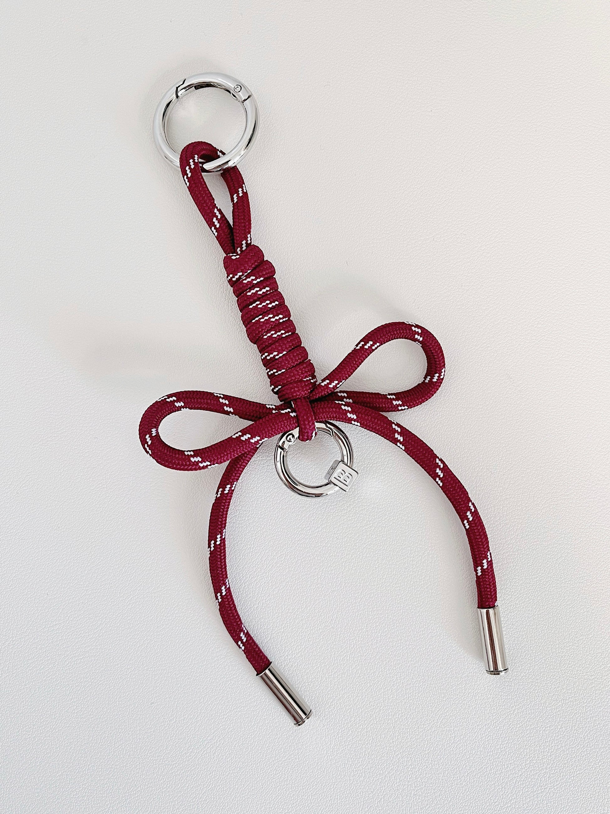 Studio product photo of a crimson red personalized ribbon bag charm with silver hardware resting on a white surface