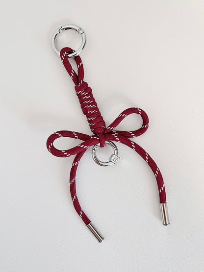 Studio product photo of a crimson red personalized ribbon bag charm with silver hardware resting on a white surface