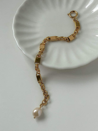 A detailed close-up showing the high-luster natural freshwater baroque pearl charm attached to the gold link architecture.