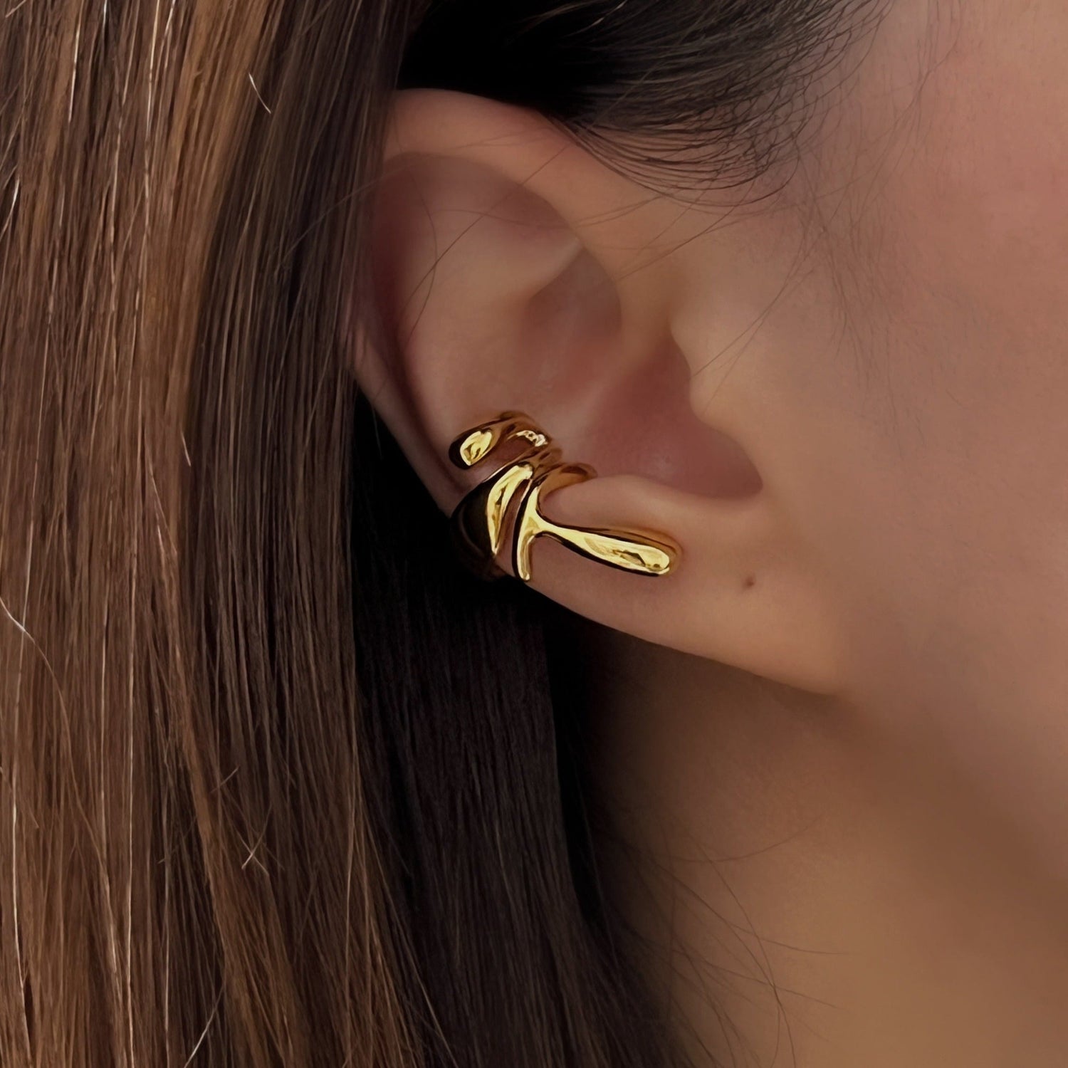 Close-up of a model's ear featuring a molten gold ear stack with no piercings.