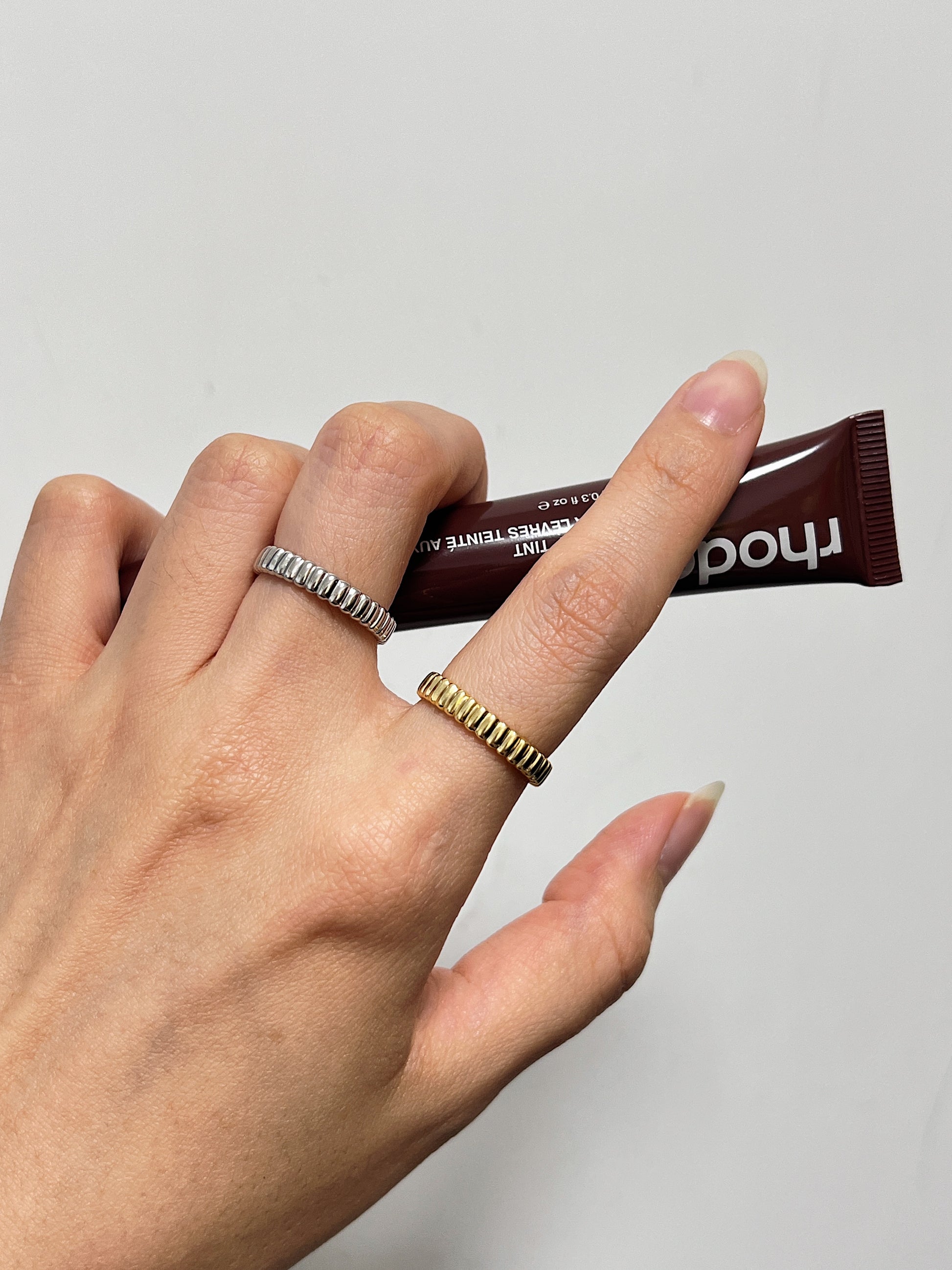 Womens hand wearing a bold textural gold ribbed ring against on a clean wall