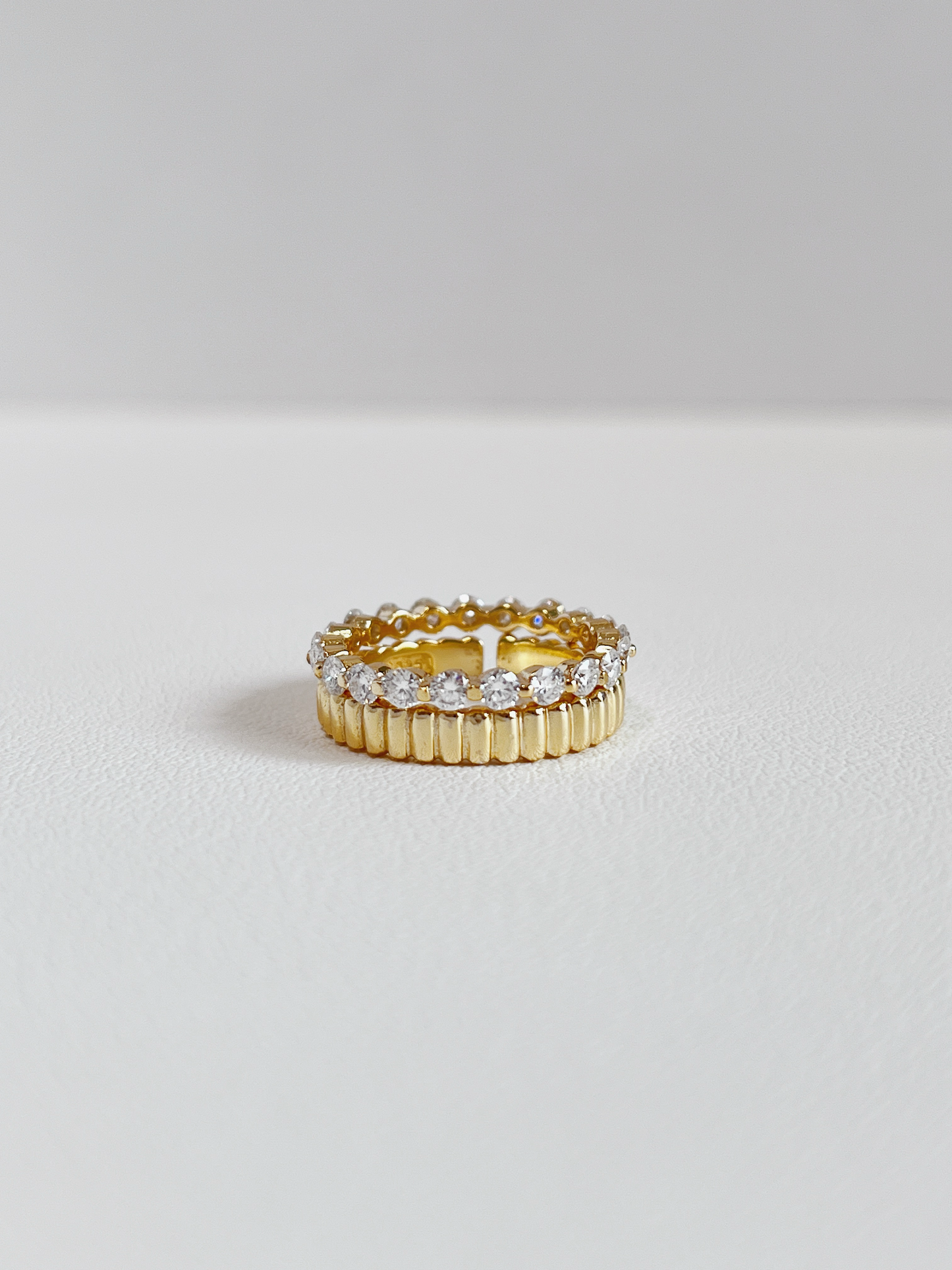 Editorial jewelry layout displaying a brilliant round cut gemstone eternity ring nested with a solid gold ridge band