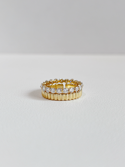 Editorial jewelry layout displaying a brilliant round cut gemstone eternity ring nested with a solid gold ridge band