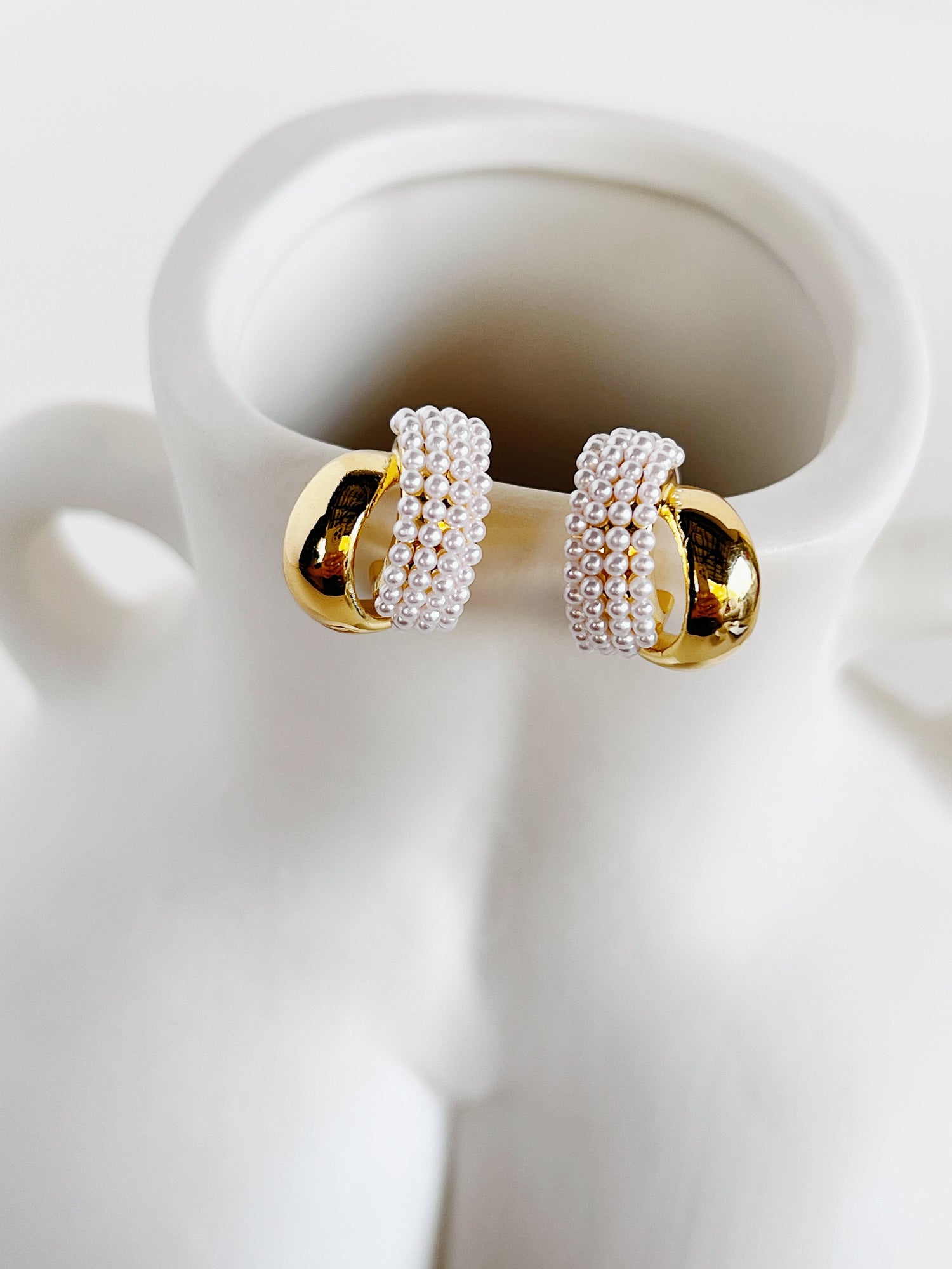 Evadne sculptural pearl crossover earrings showing dual ribbon bands on white surface