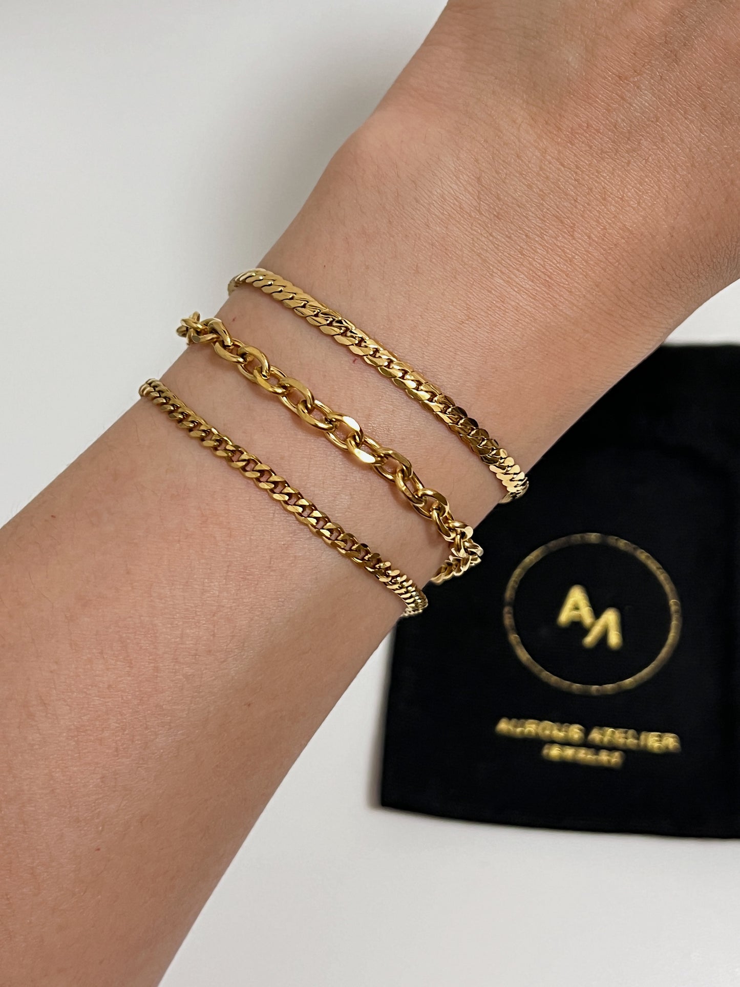 Lifestyle shot showcasing how the gold cable chain bracelet layers seamlessly with finer curb chains for an effortless uniform.