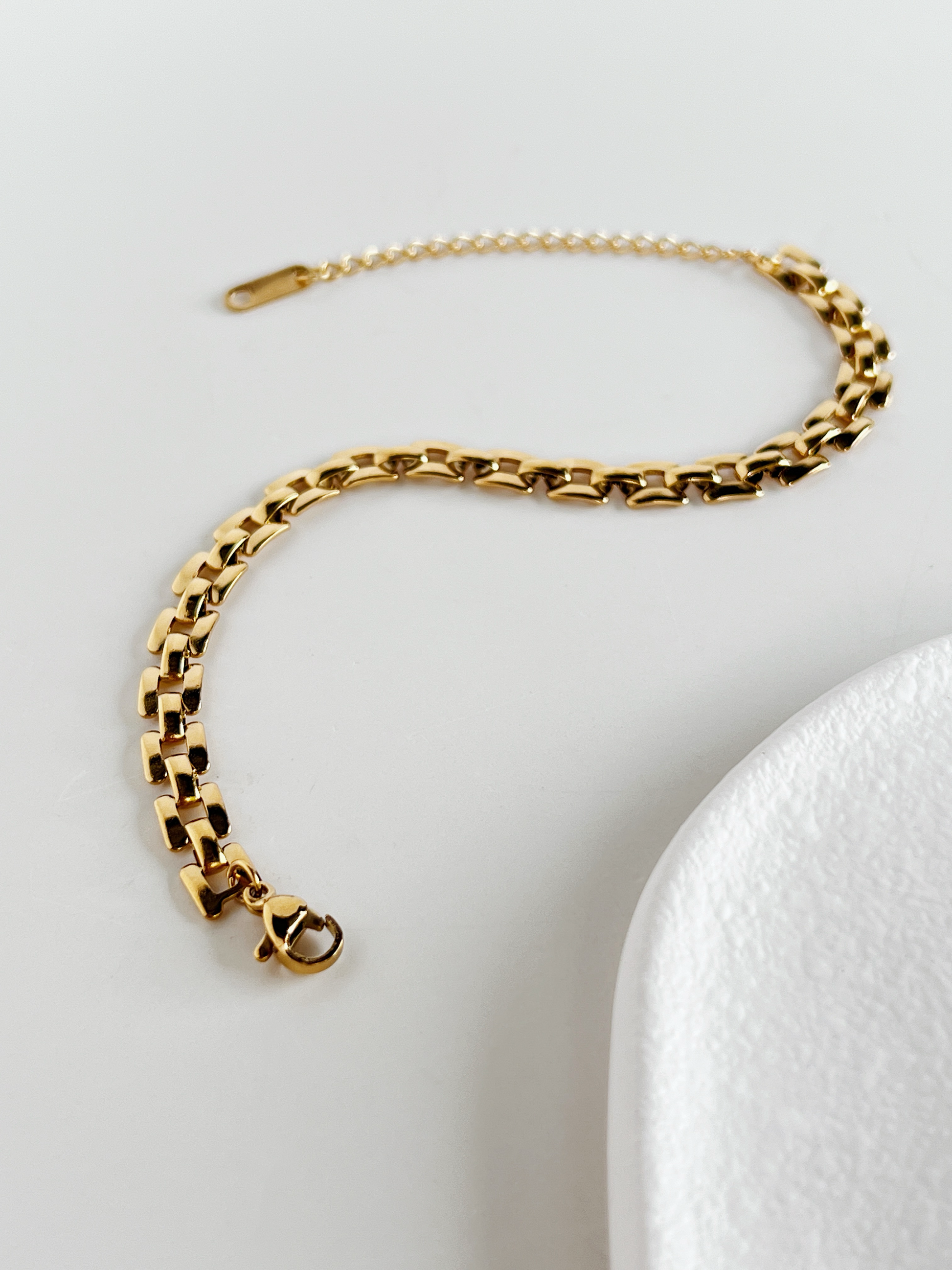 The Evie link chain curved into an elegant S shape on a white surface to show its flexible, fluid articulation.