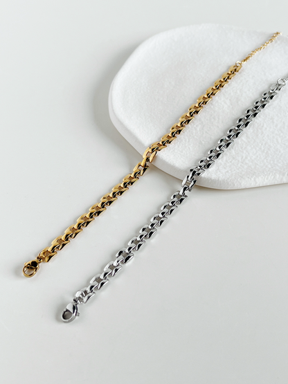 Gold and silver Evie flexible watchband link chain bracelets displayed together on a wavy white textured ceramic dish, showcasing their low-profile links.