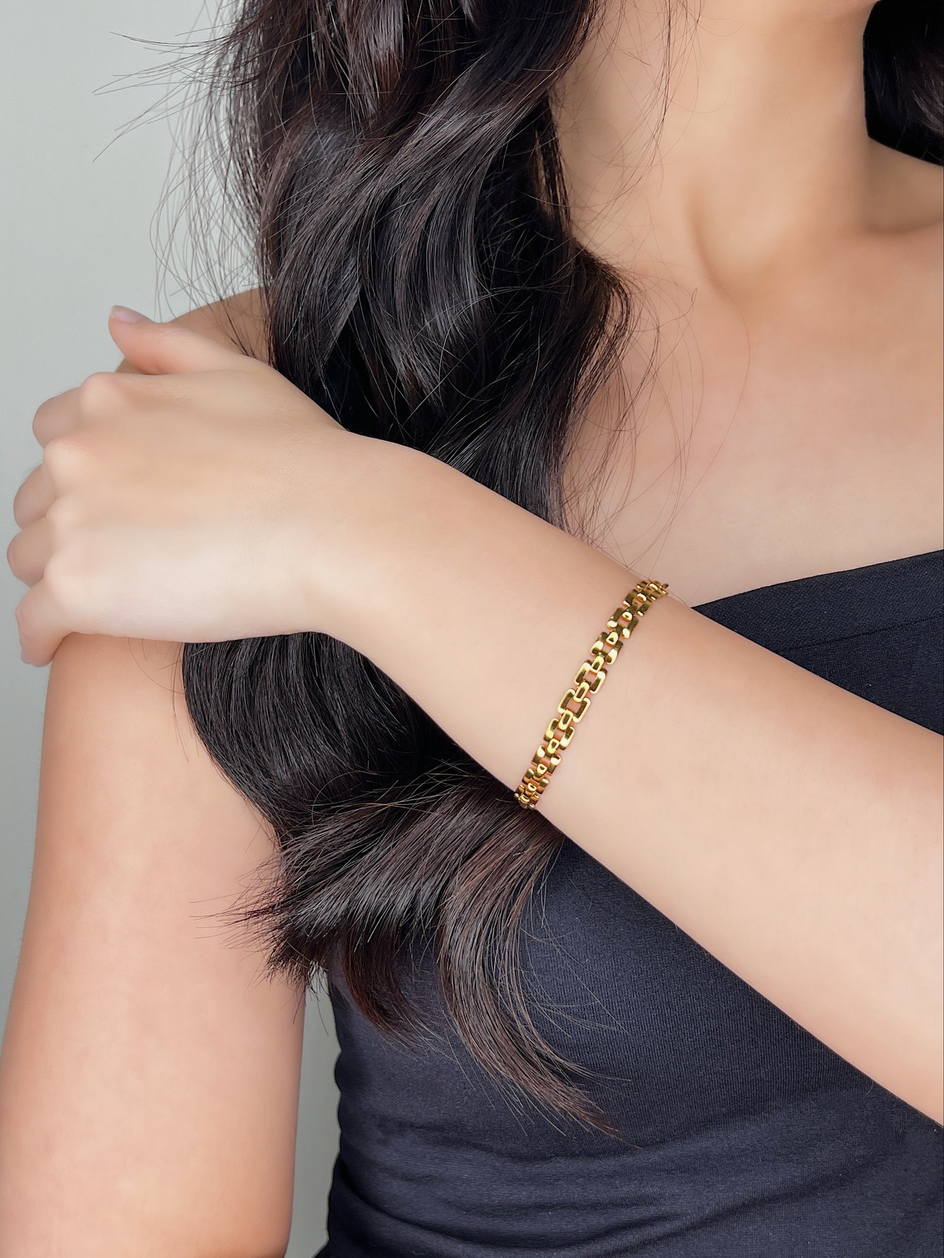 A model wearing the Evie 18K gold watchband link bracelet on her bare wrist while wearing an elegant black top