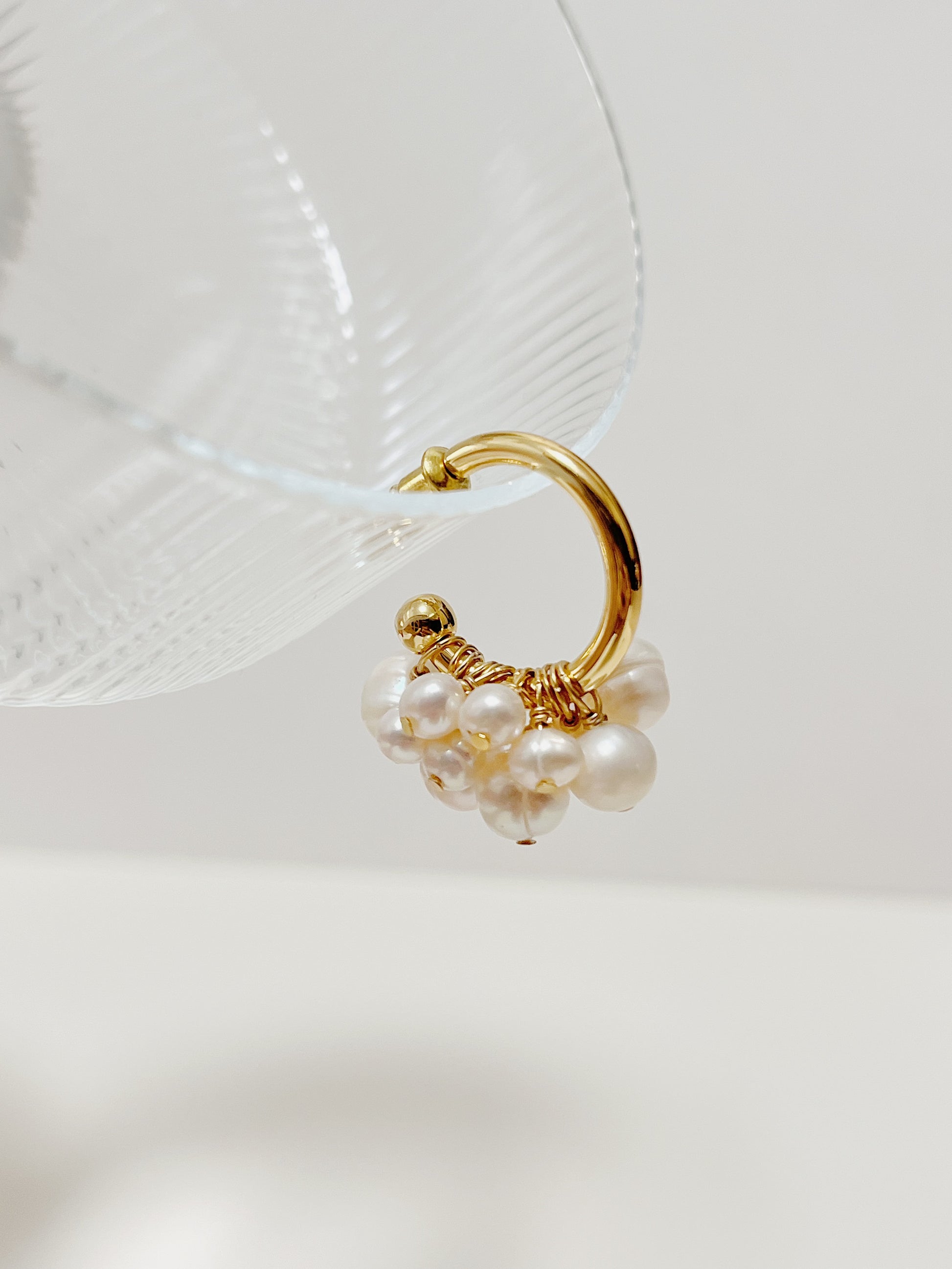 Close-up profile of the Freya luxury pearl earrings suspended elegantly on the rim of a fluted glass coupe, showing the dense hand-wired details.