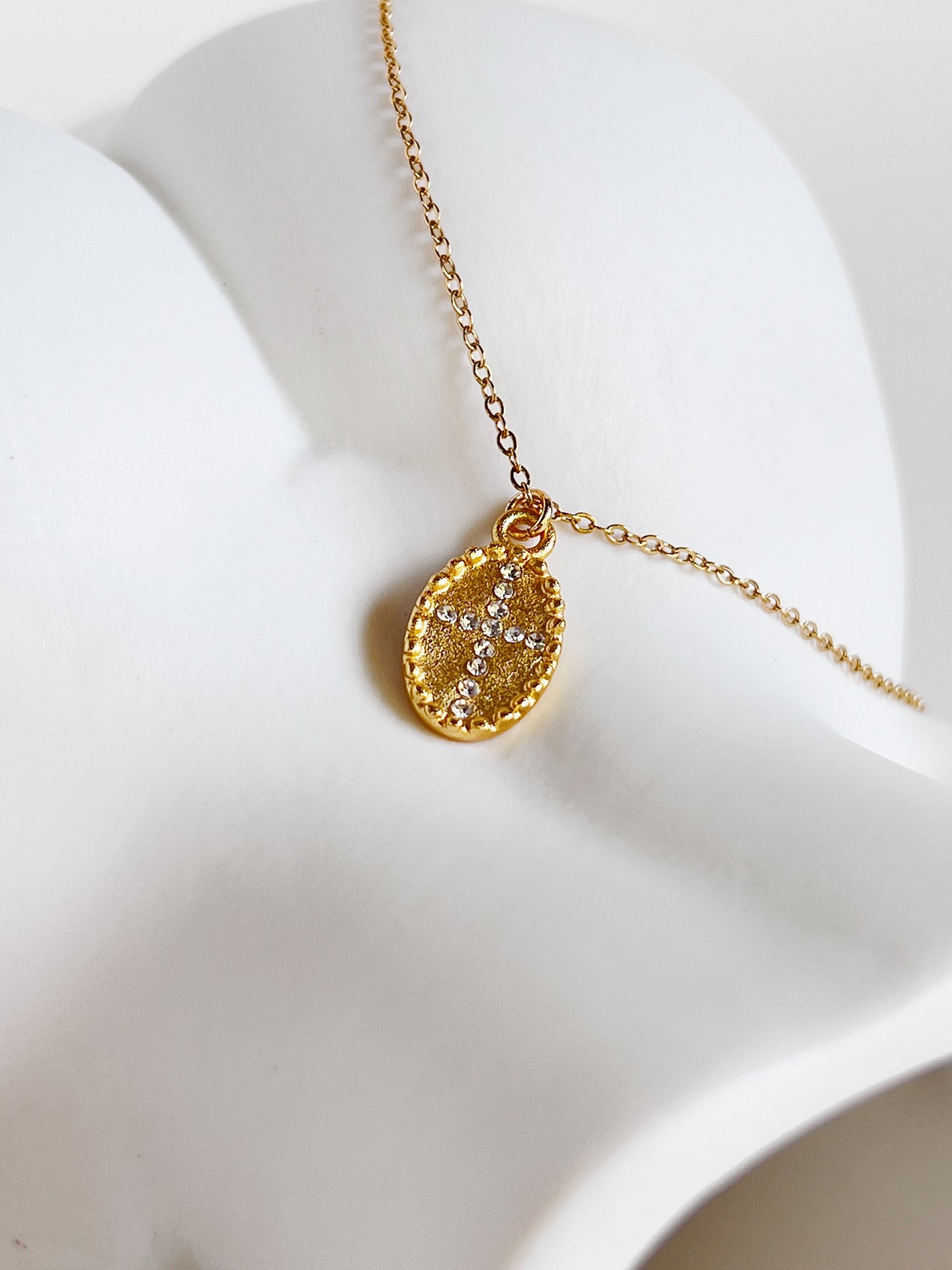 An overhead studio flatlay showcasing the gold Gianna oval cross medallion necklace resting on an sculptural white vase