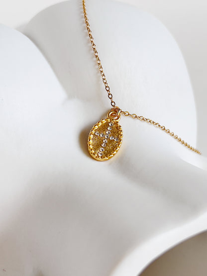 An overhead studio flatlay showcasing the gold Gianna oval cross medallion necklace resting on an sculptural white vase