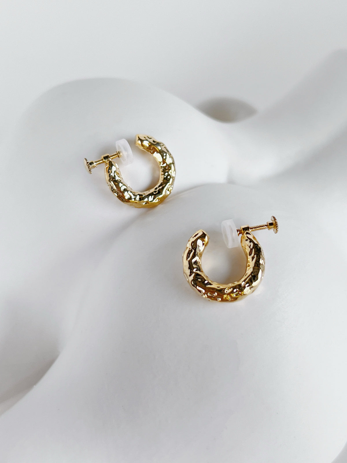 Macro close-up shot highlighting the light-refracting dimpled surface and warm 14k gold finish of the Gigi clip-on huggie hoop.
