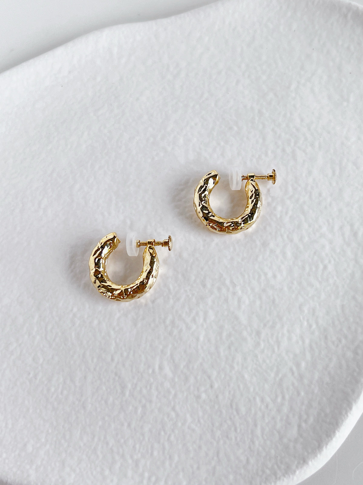 Editorial arrangement of the Gigi hammered clip-on hoops resting on an ivory dish for capsule wardrobe jewelry lovers.