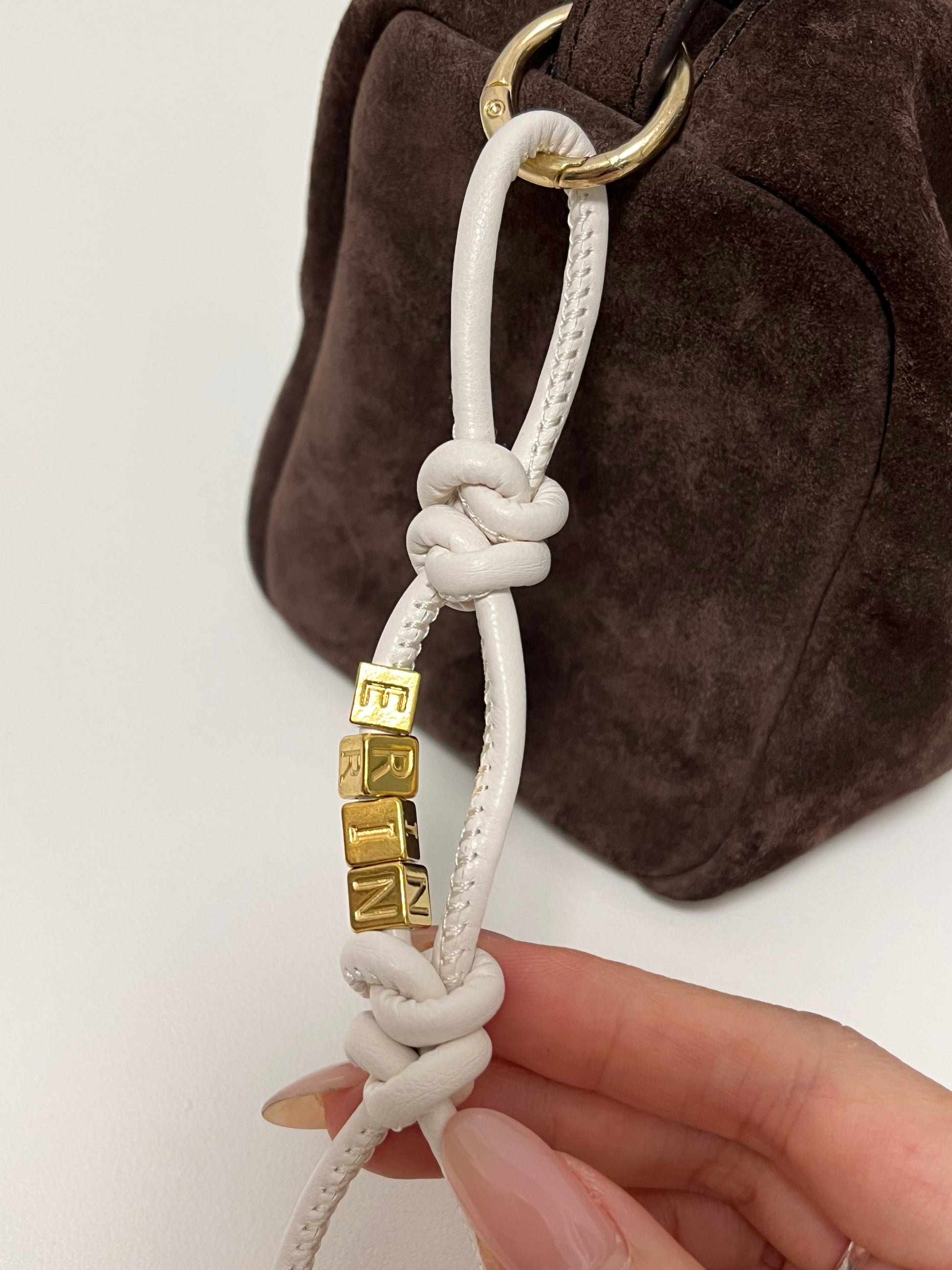 White leather initial charm with gold beads.