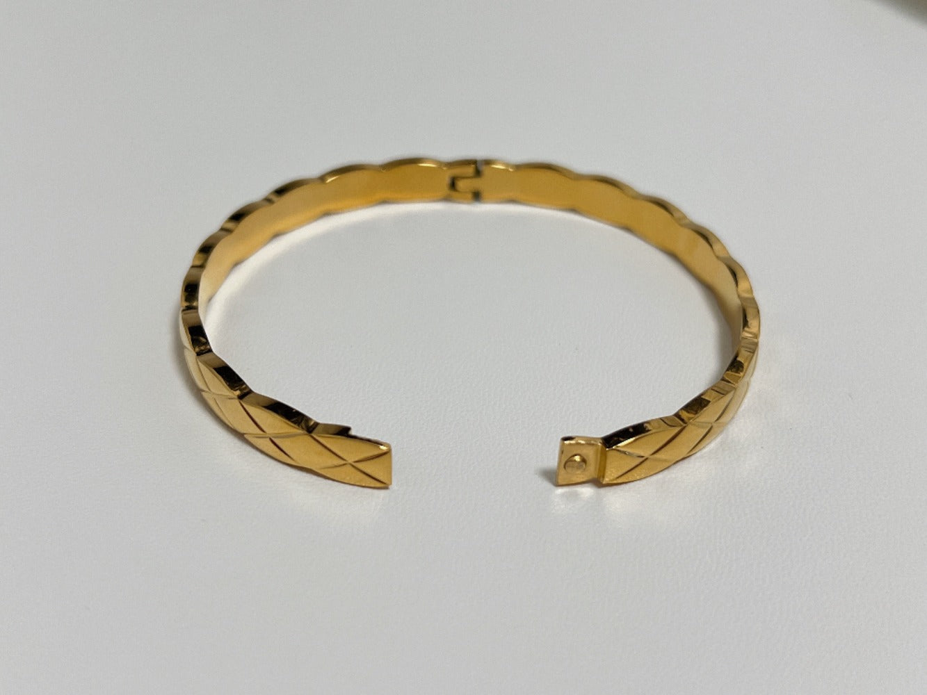 A top-down view of the gold Corin quilted hinged bangle open, displaying the high-security side hinge and seamless flush tension locking clasp design.