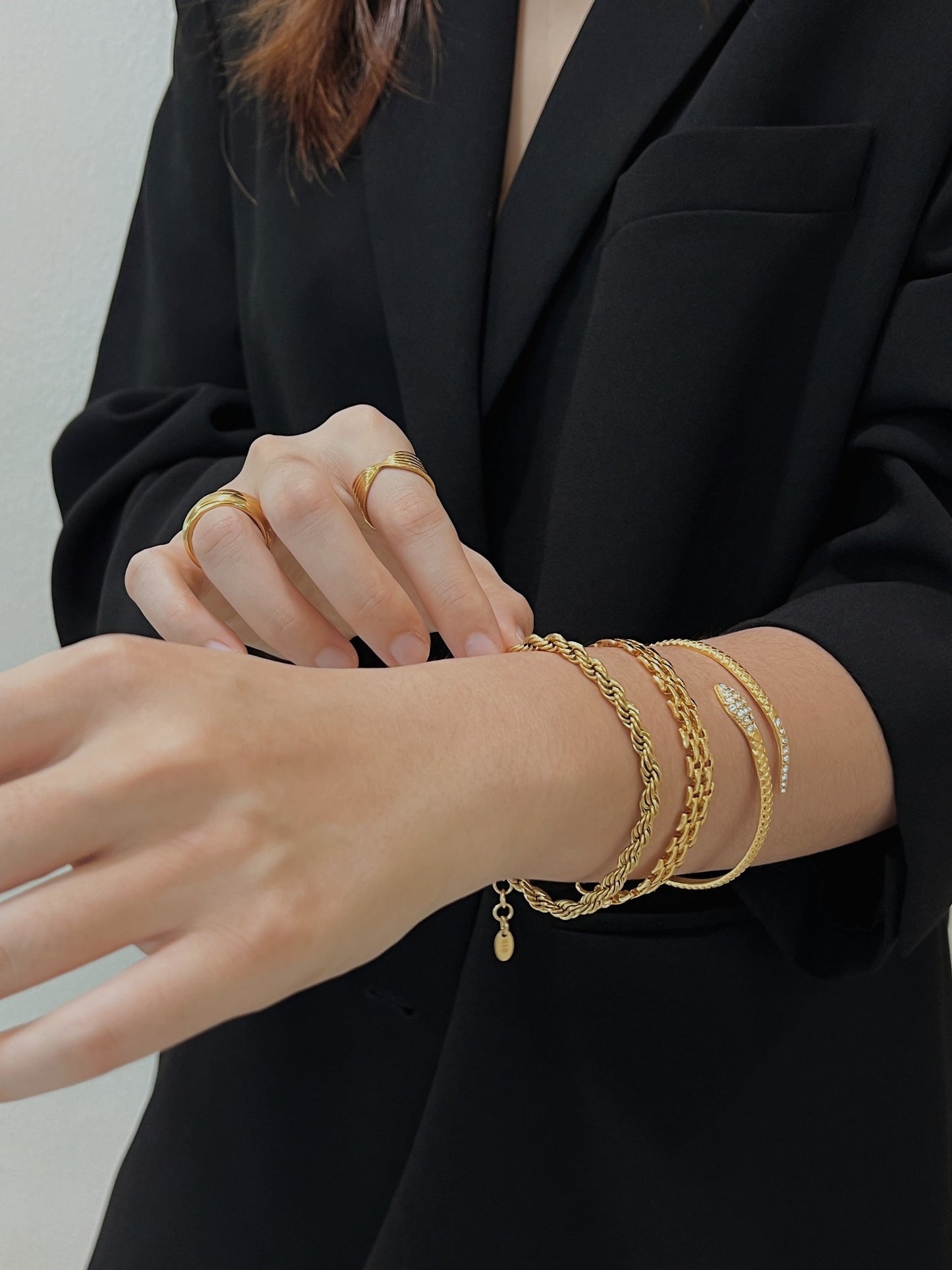 A wrist stack close-up showing the Cali 5mm gold twisted rope bracelet layered with textured gold cuffs.