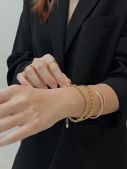 A wrist stack close-up showing the Cali 5mm gold twisted rope bracelet layered with textured gold cuffs.