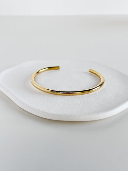 Minimalist presentation of the Ines gold stainless steel cuff bracelet centered on a white display tray, highlighting its clean open-ended silhouette.