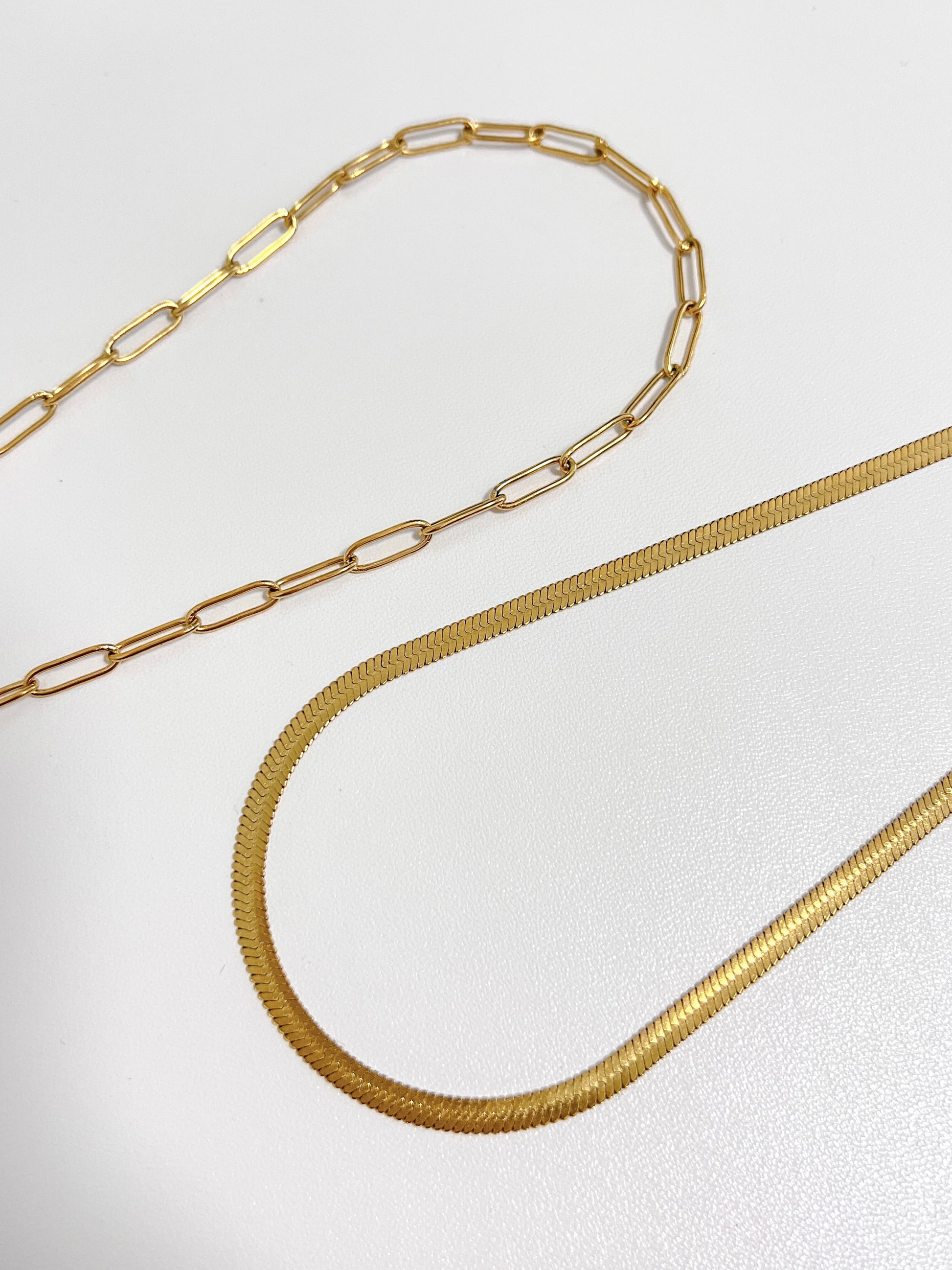 Close-up studio shot of a high-shine gold tone precious metal selection featuring elongated geometric loop chains and herringbone chain