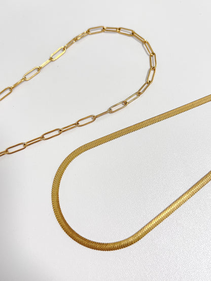 Close-up studio shot of a high-shine gold tone precious metal selection featuring elongated geometric loop chains and herringbone chain