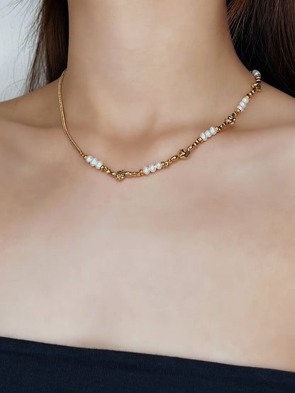 A side-angled portrait of a model wearing the Greta asymmetric necklace. The shot beautifully illustrates how the minimalist gold chain sits on one side of the neck, while the strand of organic freshwater pearls and molten gold beads sits on the other, creating a unique visual balance.