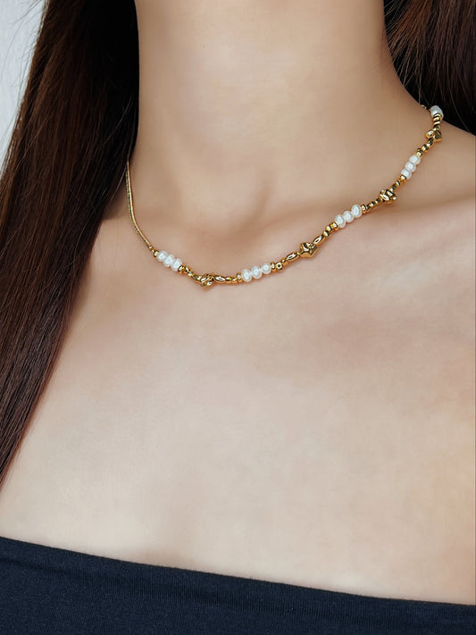 Model wearing Greta asymmetric necklace showing the contrast between a sleek gold chain on one side and a textured strand of organic white pearls and crushed gold metallic accent beads