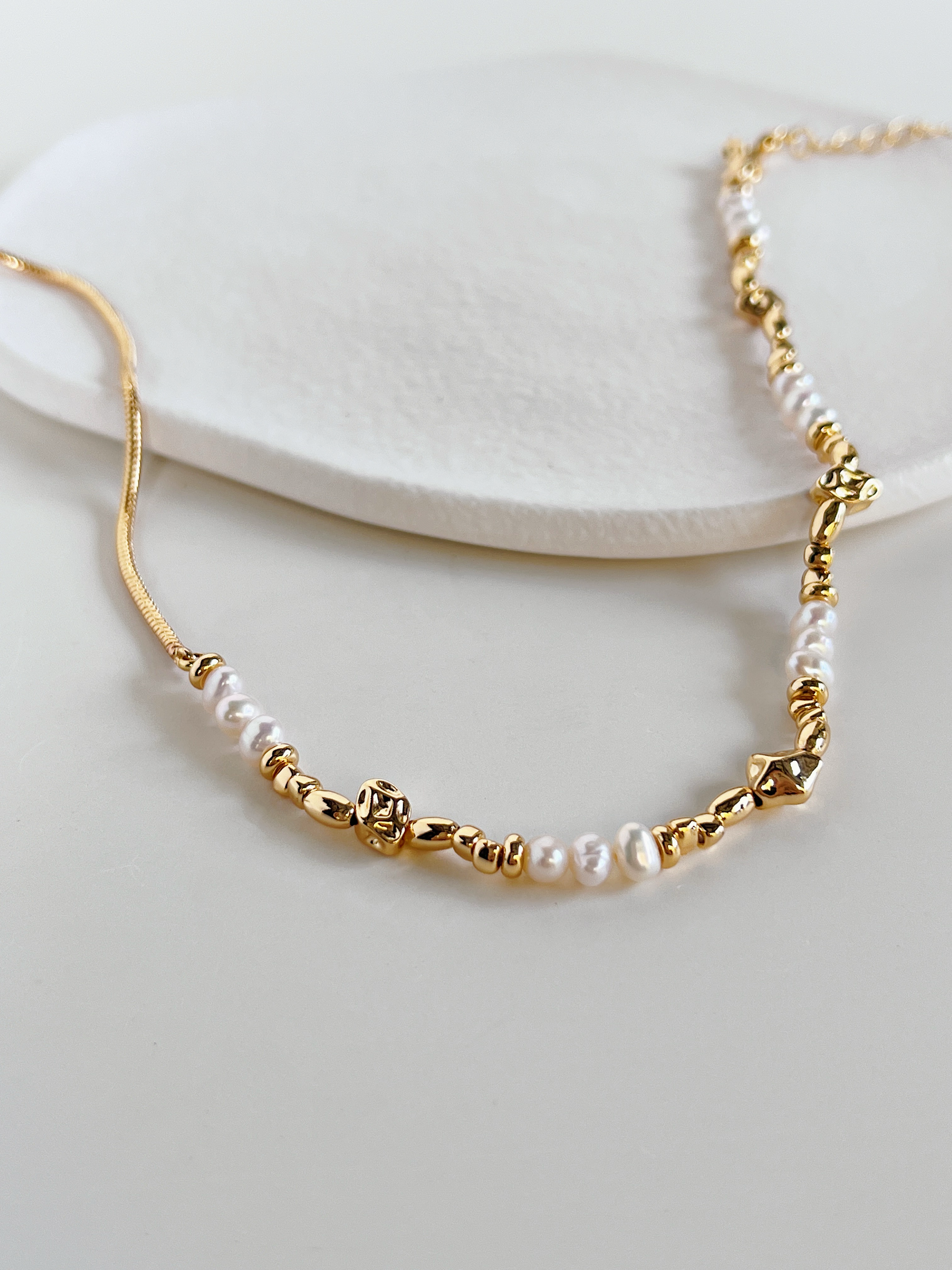 Macro product photography of Greta necklace highlighting the high-shine finish of textured organic gold geometric elements and genuine mini freshwater pearls.