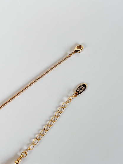 A high-resolution close-up of the Greta necklace's closure system, featuring a polished gold lobster clasp, a delicate extender chain, and a distinct oval gold tag engraved with the word "Handmade." This shot emphasizes the artisan quality of the piece.