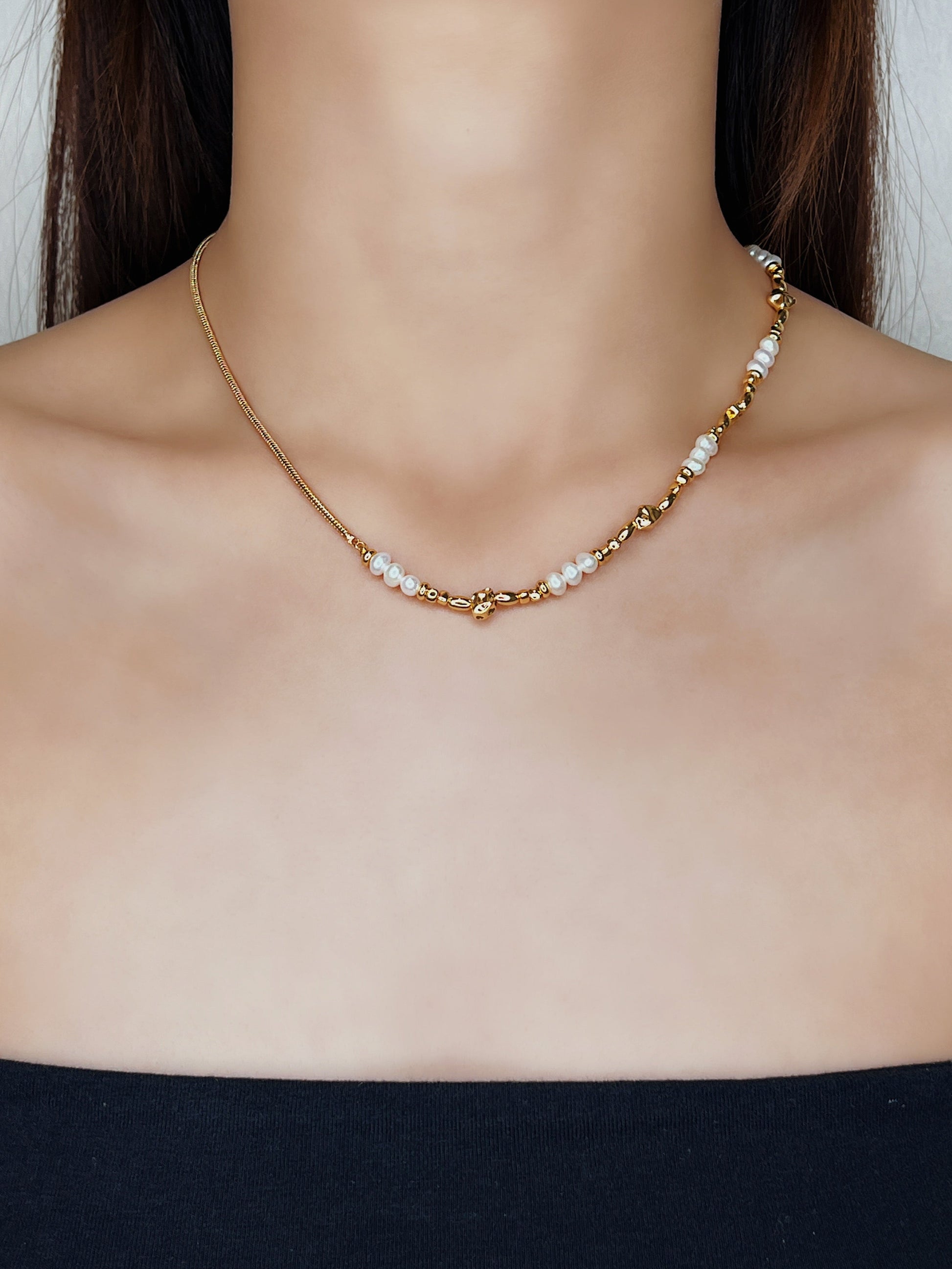 Editorial on-model view of Greta demi-fine necklace highlighting the asymmetrical blend of minimalist gold snake chain and fluid, baroque pearls styled for a modern luxury look.