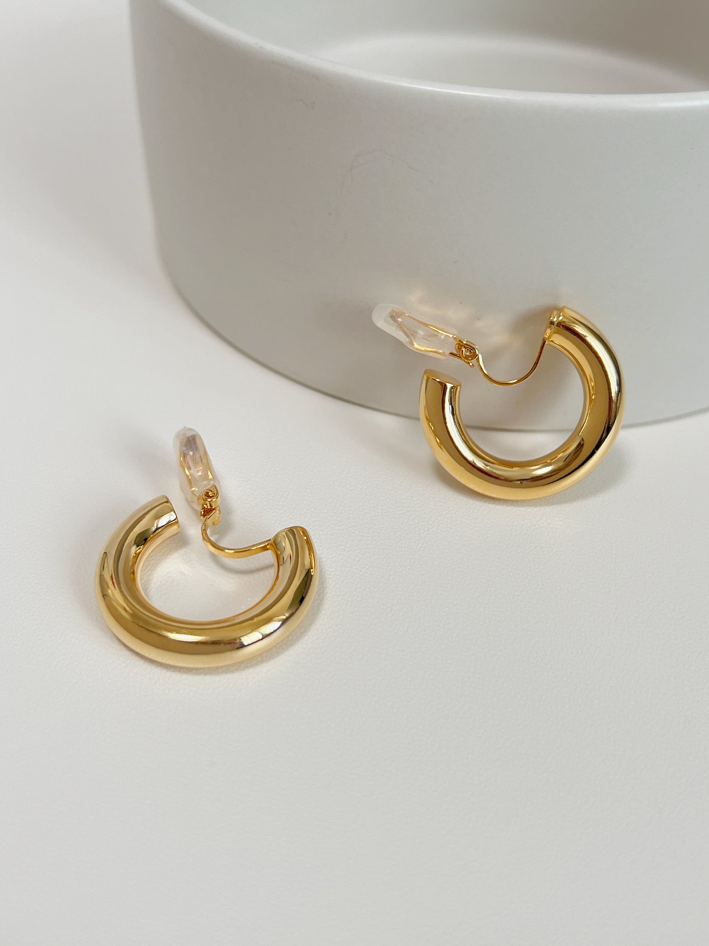 Studio product layout of gold harper clip on hoop earrings resting on a clean white display surface