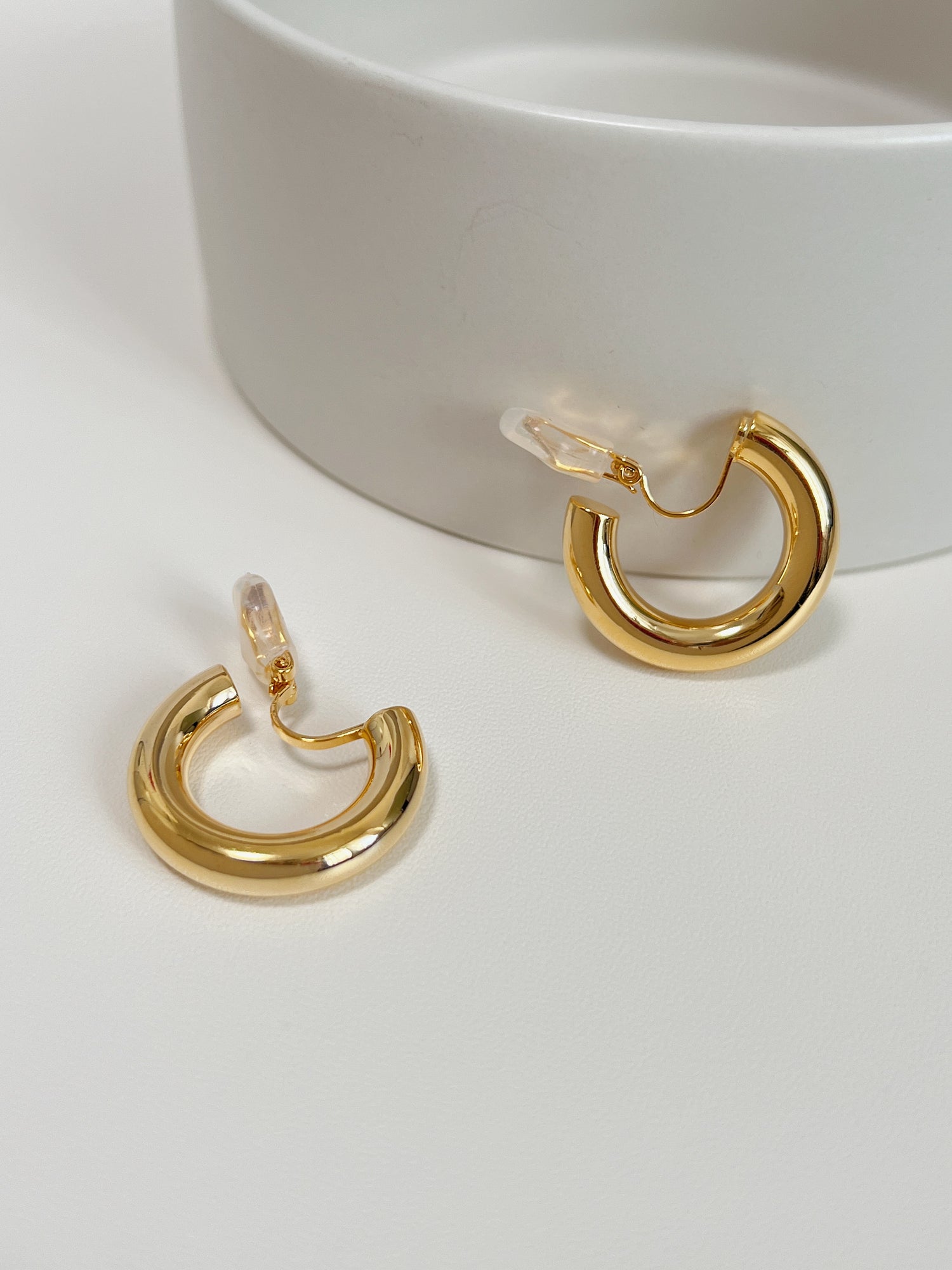 Studio product layout of gold harper clip on hoop earrings resting on a clean white display surface