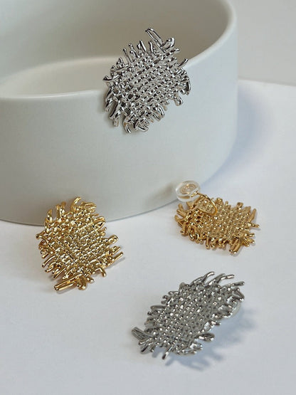 Close up view comparing 18K gold plated and rhodium plated Hazel textured earrings on white surface