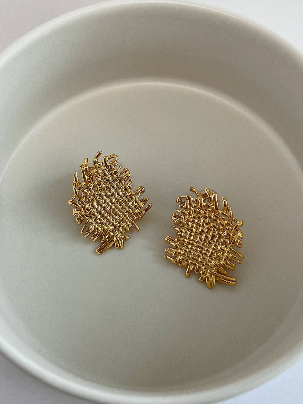 Pair of 18K gold plated Hazel woven textured clip-on earrings on neutral background