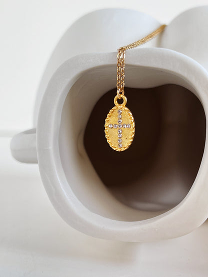 Side angle product photography showing the solid core 18k gold PVD cross medallion as it drapes along the curve of a minimalist body vase