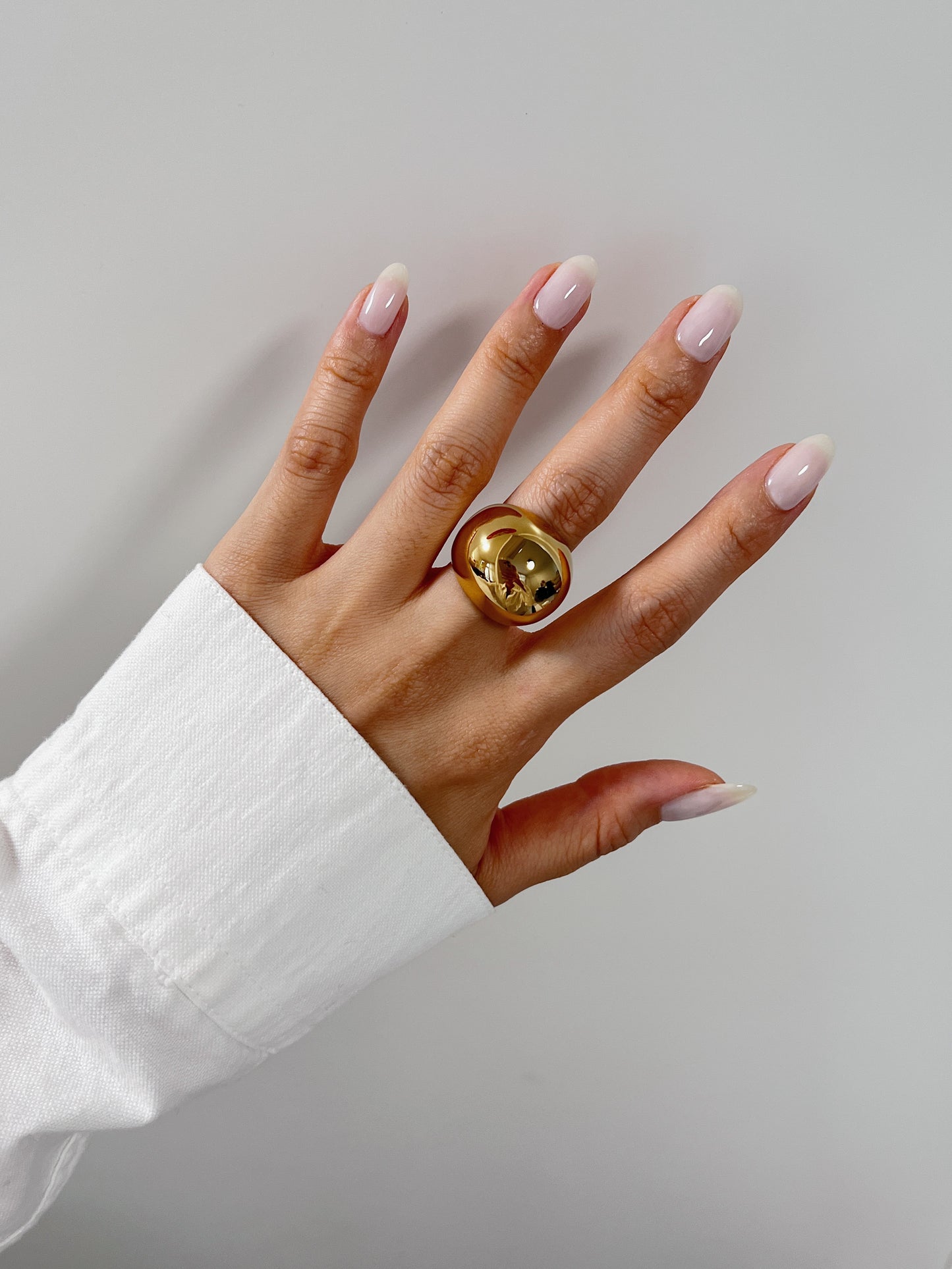 High-mirror gold sculptural ring catching light on model's finger