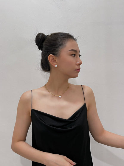 Profile lookbook view of a model wearing a sculptural gold rice bead necklace with a single round pearl drop paired with a minimalist black satin slip dress