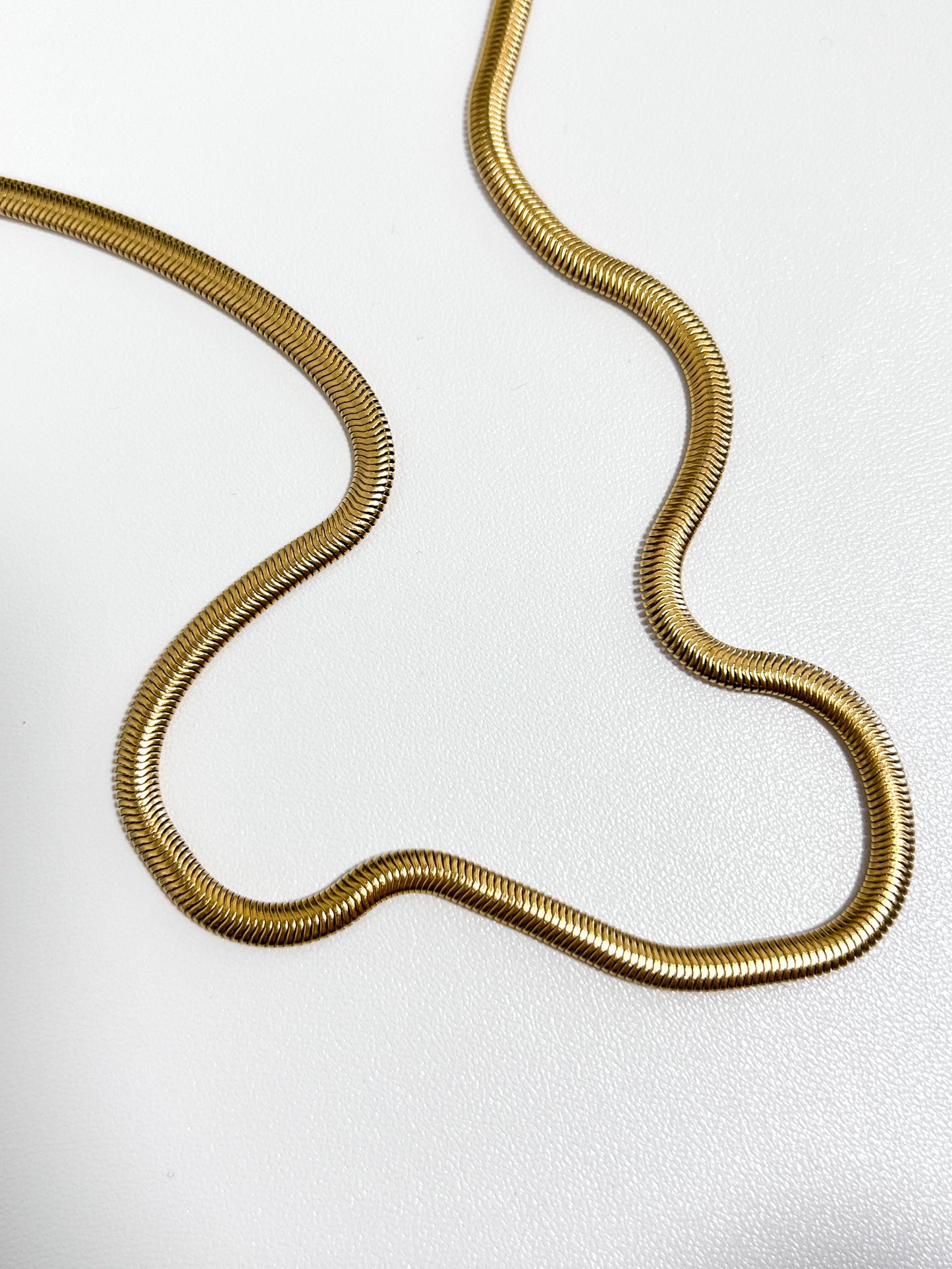 High luster flat gold necklace casting smooth light reflections on a minimalist catalog backdrop