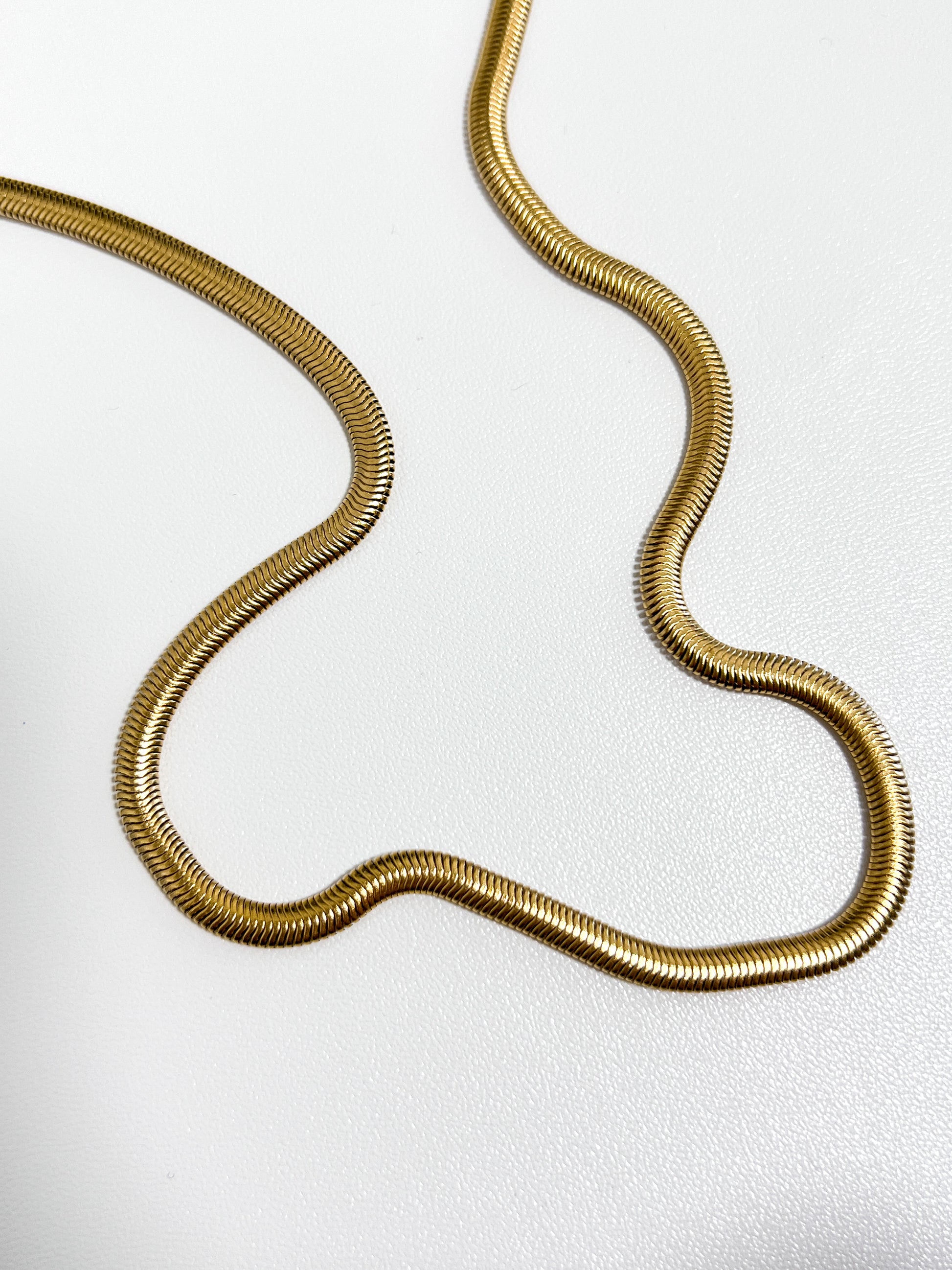 High luster flat gold necklace casting smooth light reflections on a minimalist catalog backdrop